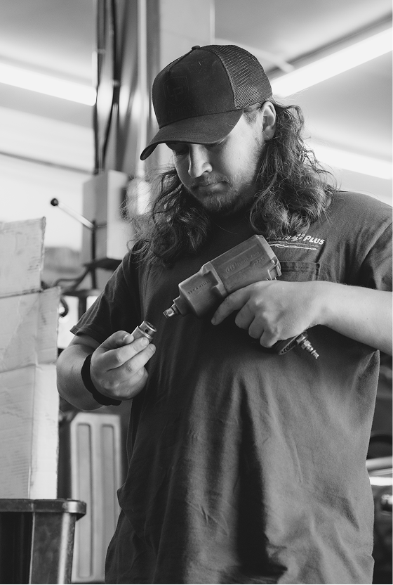 Mechanic with a mullet wearing a cap, working on a tool in a workshop. Black and white.