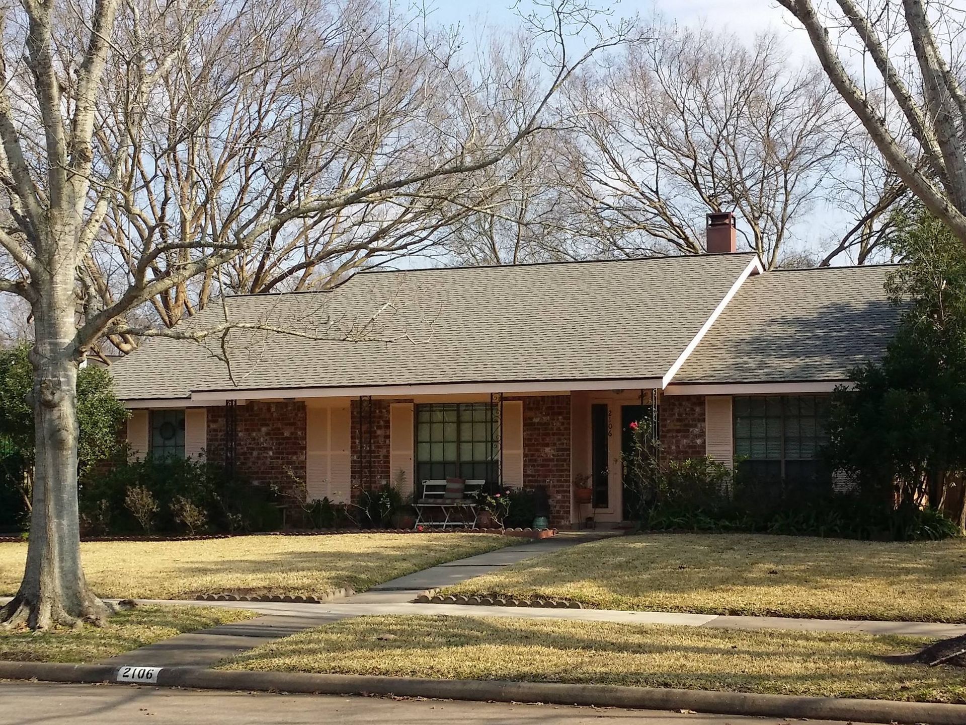 A brick house with a gray roof sits on a sunny day