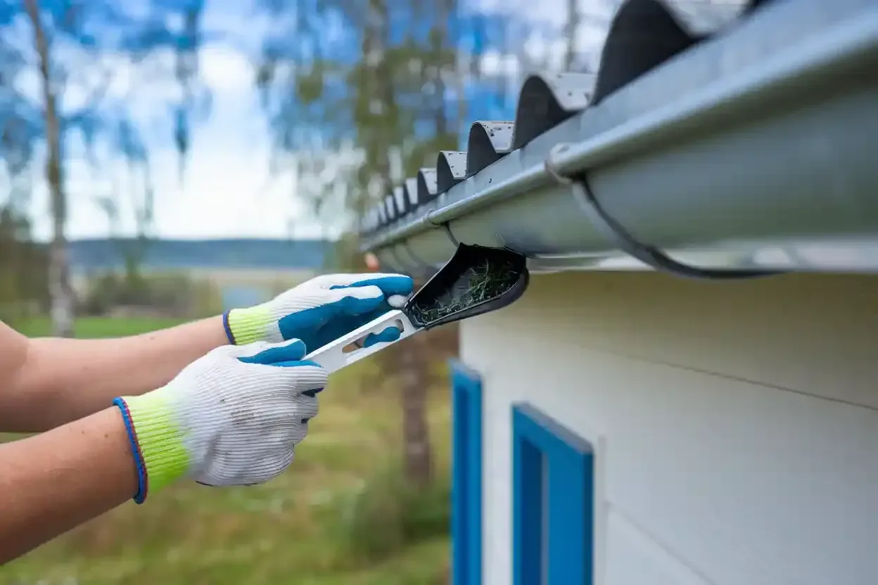A person is cleaning a gutter on the roof of a house.