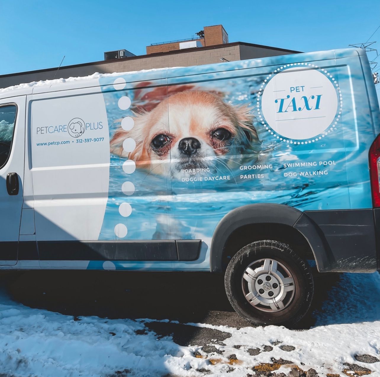 A pet care plus van with a picture of a dog on the side is parked in the snow in dog daycare