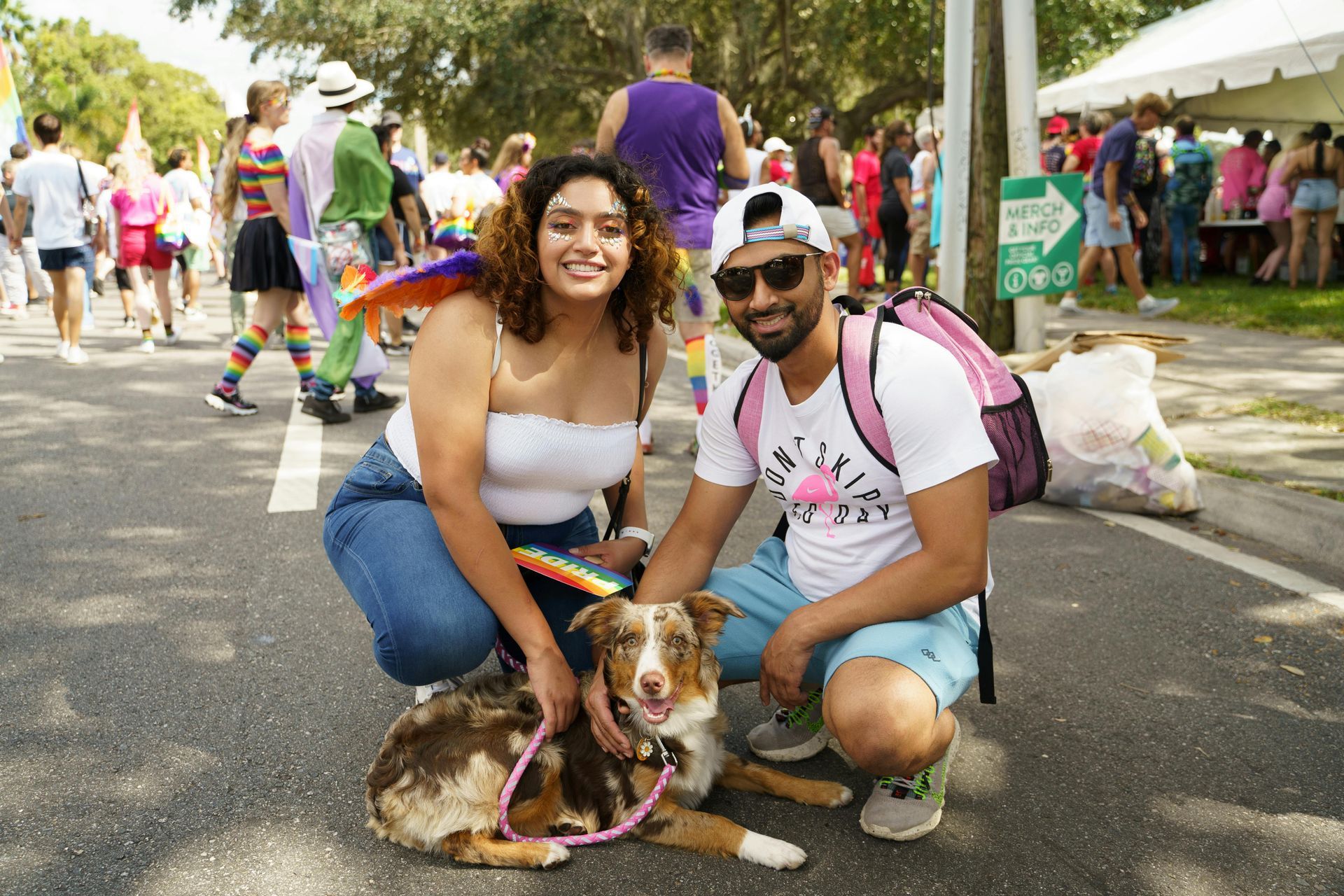 A man and a woman are kneeling down next to a dog on the street.