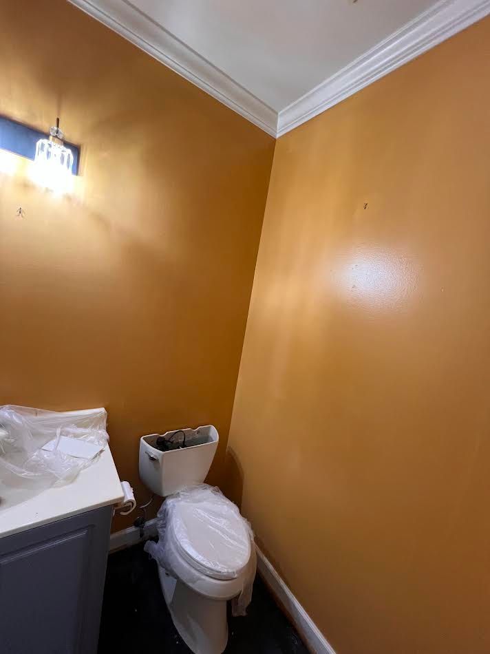 Small bathroom with orange walls, toilet, sink, and a wall light.