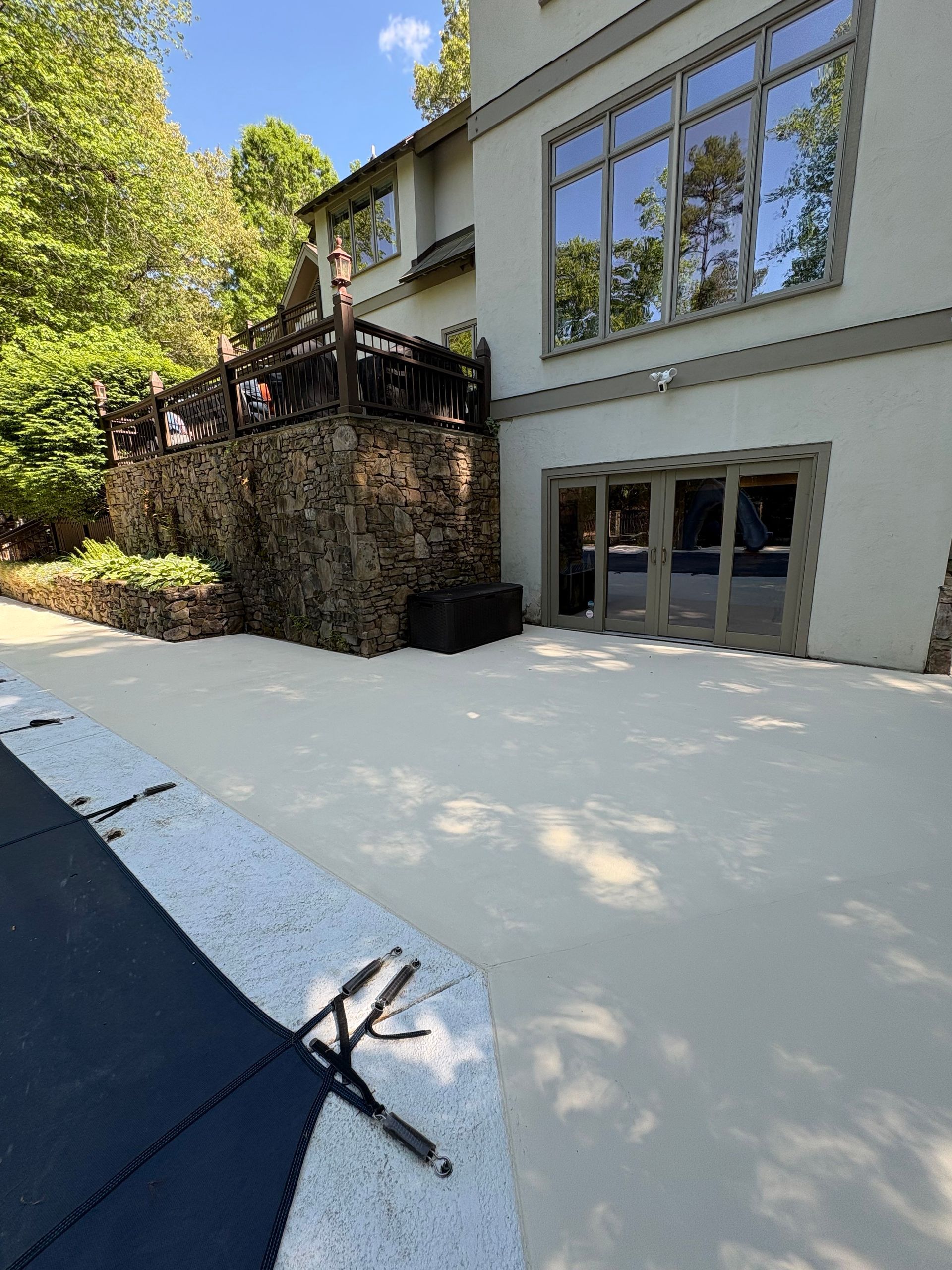 Modern building exterior with large windows, stone retaining wall, and sloped driveway in sunlight