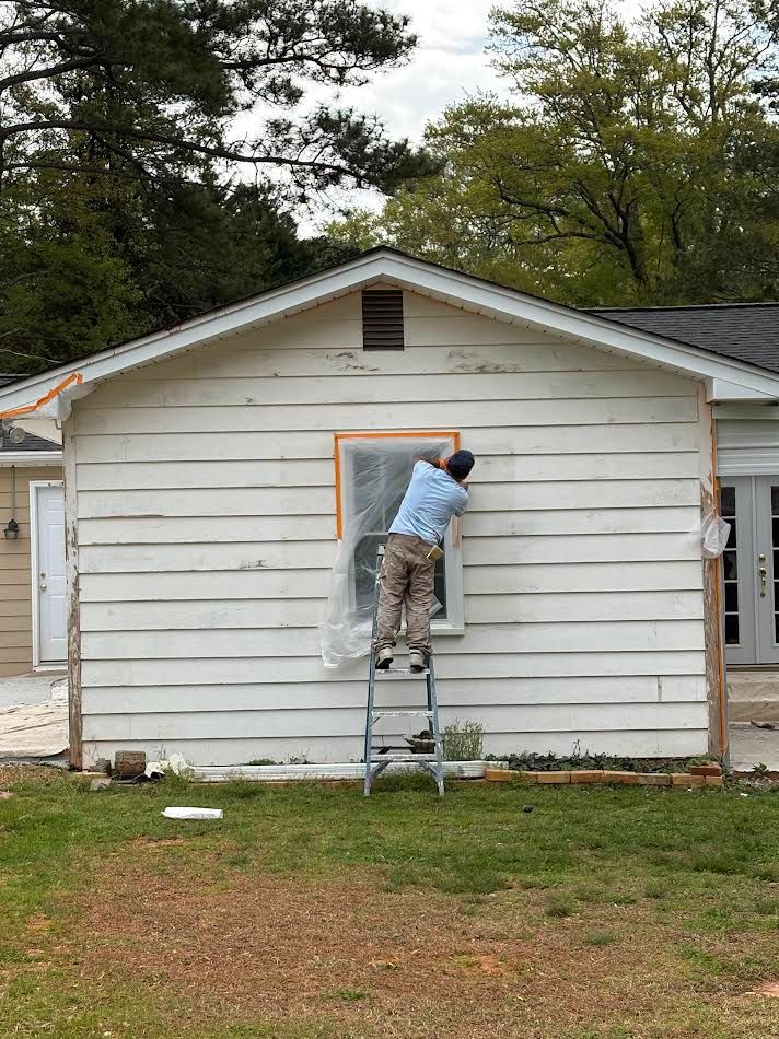 Person on a ladder painting a small house window trim orange