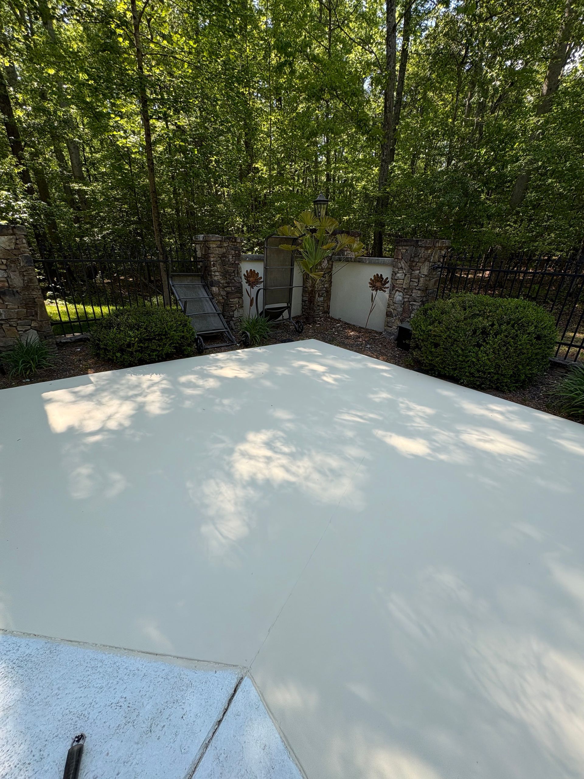 Concrete patio beside brick garden walls and dense green trees, viewed from a bright outdoor terrace.