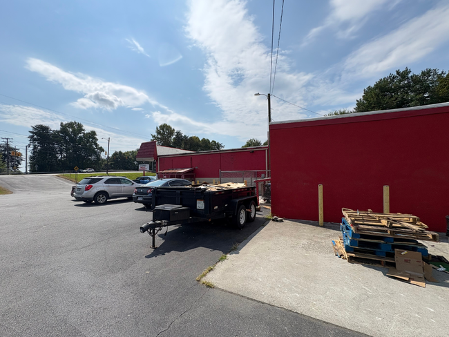 A trailer parked in a paved lot next to a red building, with a stack of wooden pallets in the foreground.