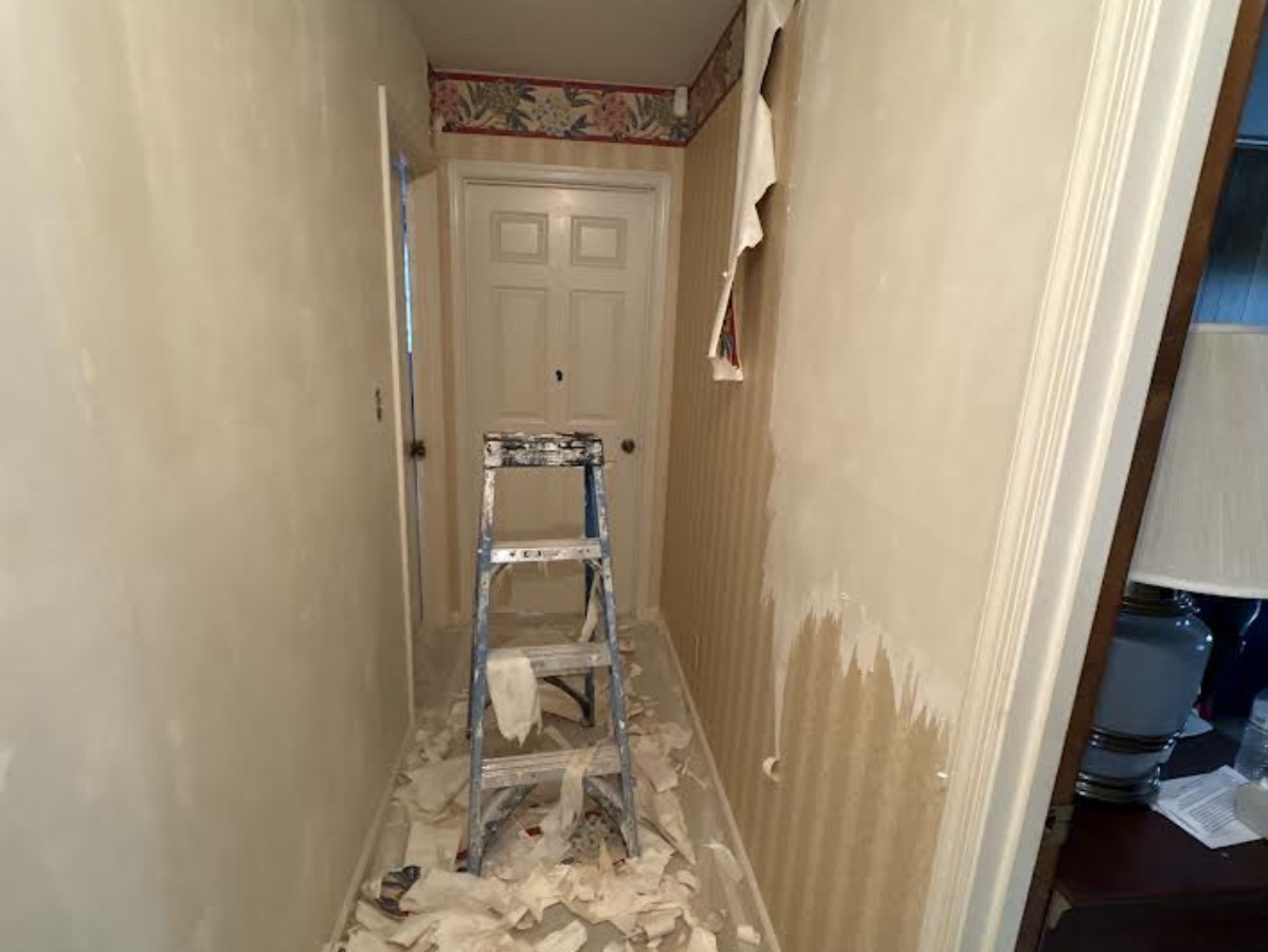 Narrow hallway under renovation with a step ladder, paint tools, and protective covering on the floor