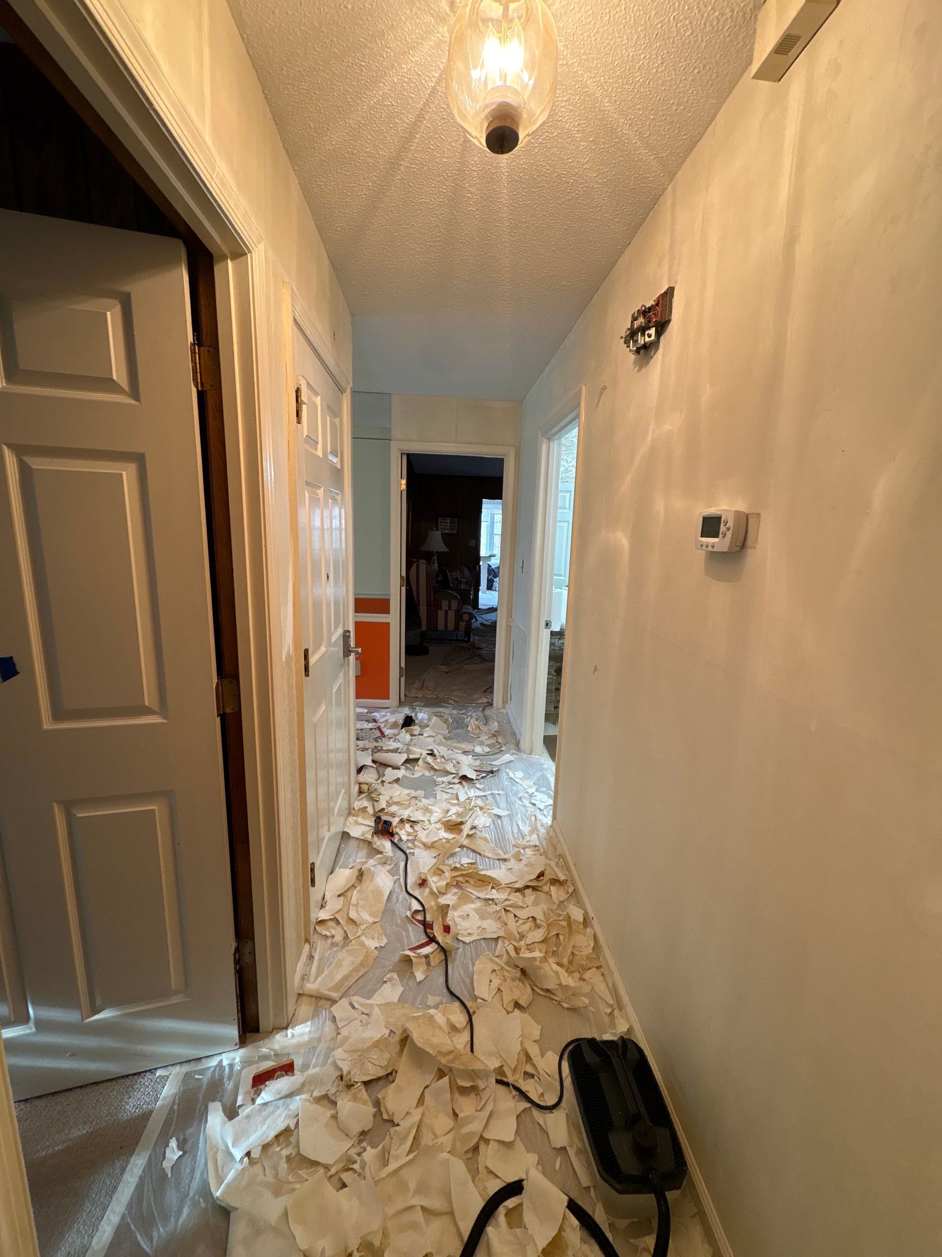 Damaged hallway with debris-covered floor, exposed walls, and a doorway at the end.