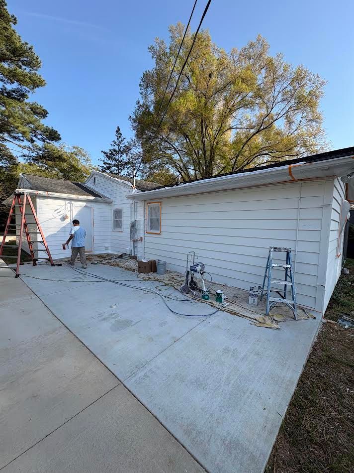 Driveway beside white garage with ladder, tools, and a person working near the house under a blue sky