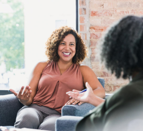 Two people sitting in armchairs, having an engaged conversation in a sunlit room with exposed brick walls.