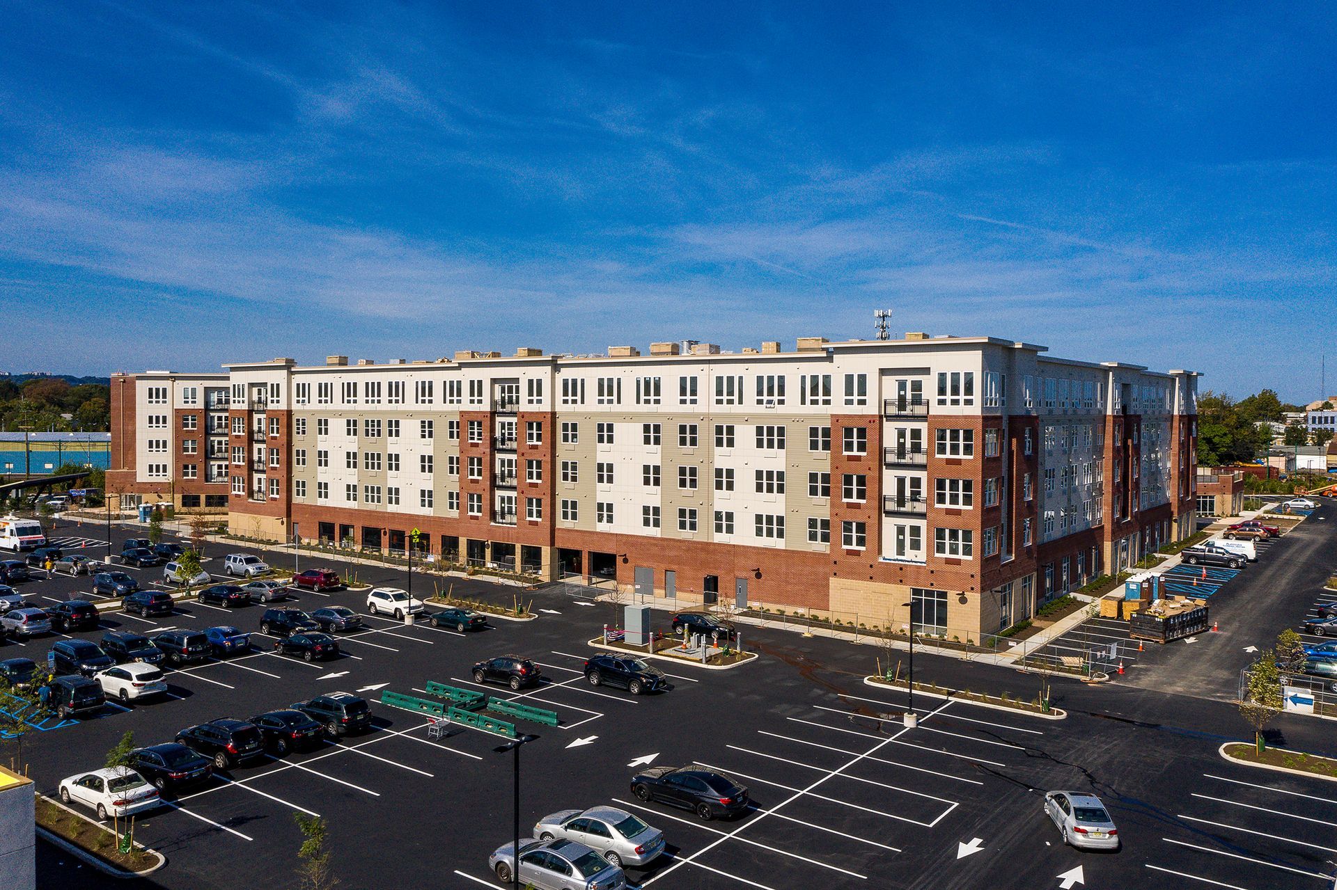 Multi-story apartment building with a large parking lot, blue sky.