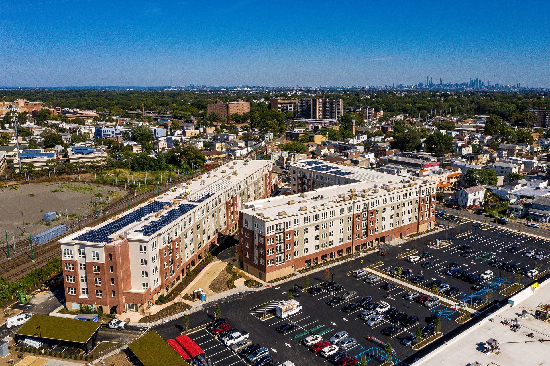 Aerial view of a U-shaped apartment building with a large parking lot, and city skyline in the distance.