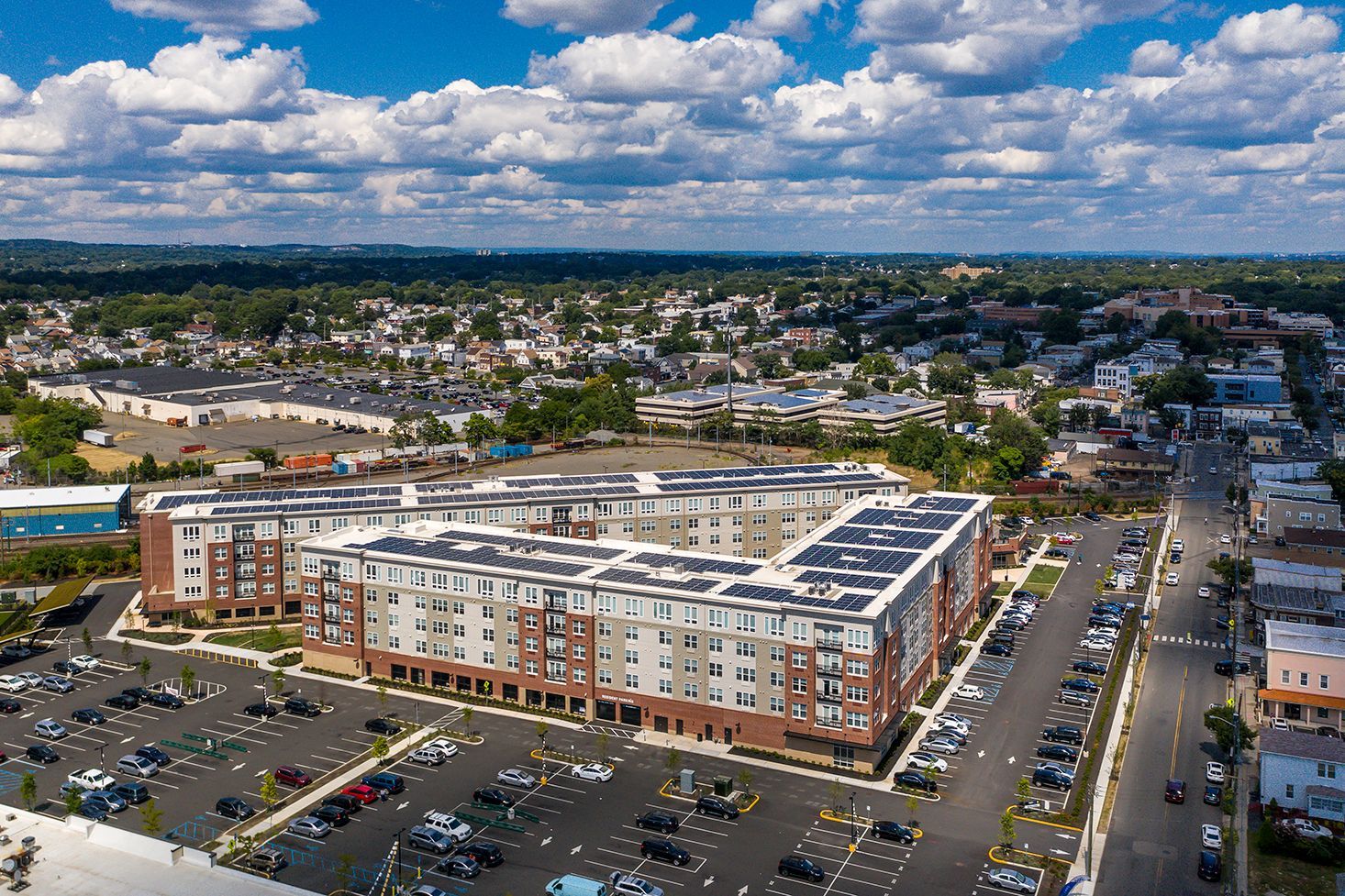Aerial view of a modern apartment complex with a large parking lot on a sunny day.