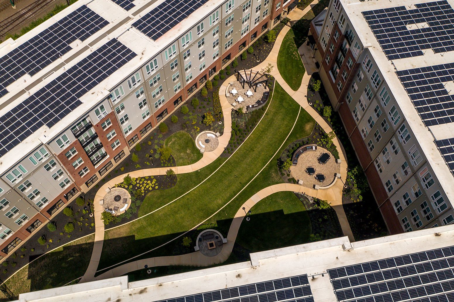 Aerial view of a multi-story building with solar panels on the roof and a central courtyard with walkways and greenery.
