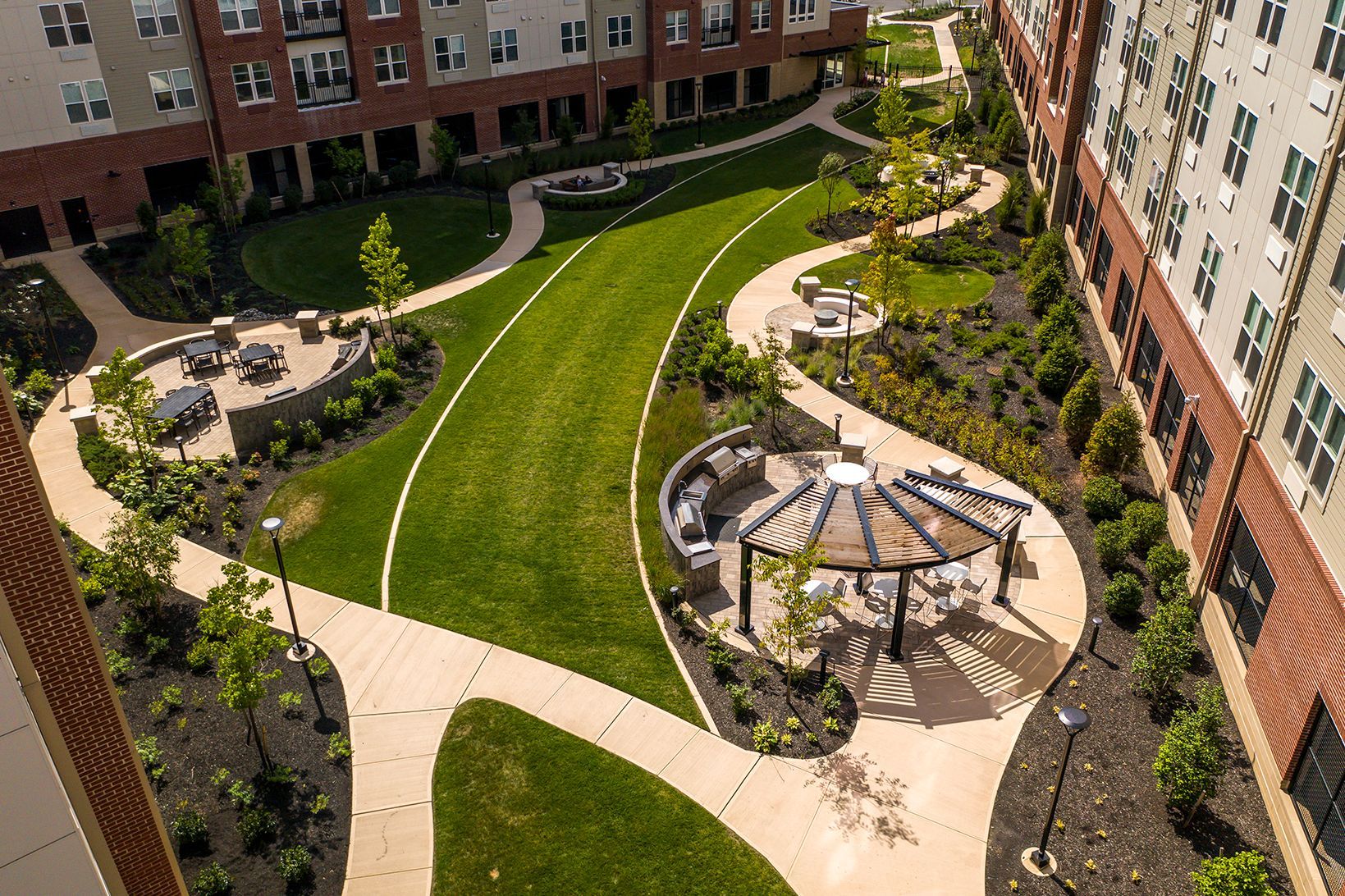 Aerial view of an apartment courtyard with walking paths, seating areas, lawn, and a pergola.