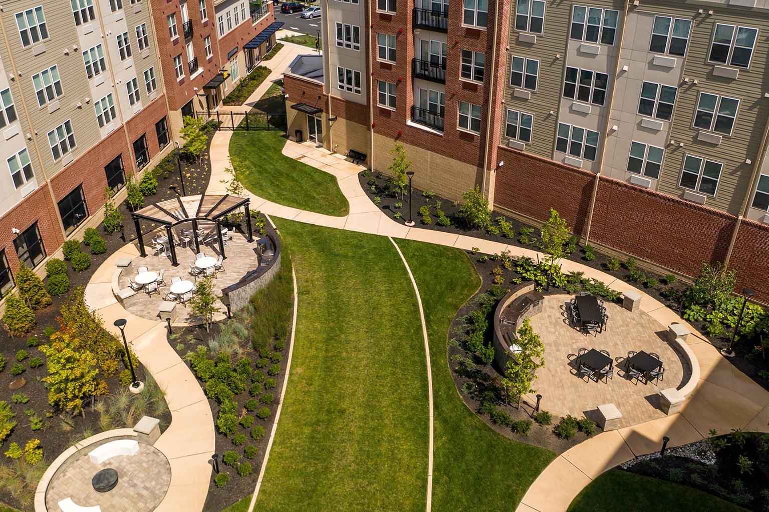 Courtyard with green lawn, curved walkways, seating areas, and apartment buildings.