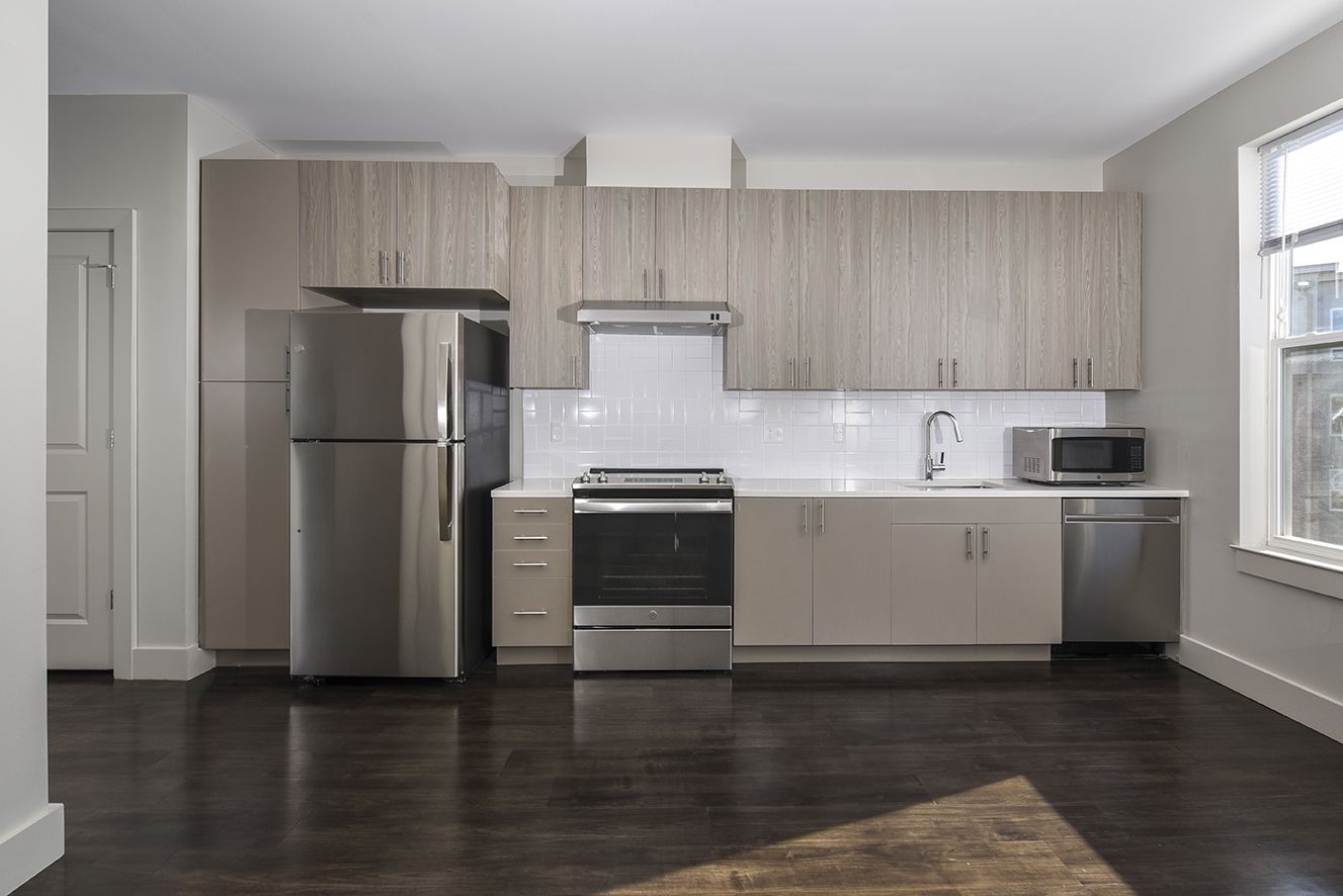 Modern kitchen with stainless steel appliances, light wood cabinets, white countertops, and dark hardwood floors.