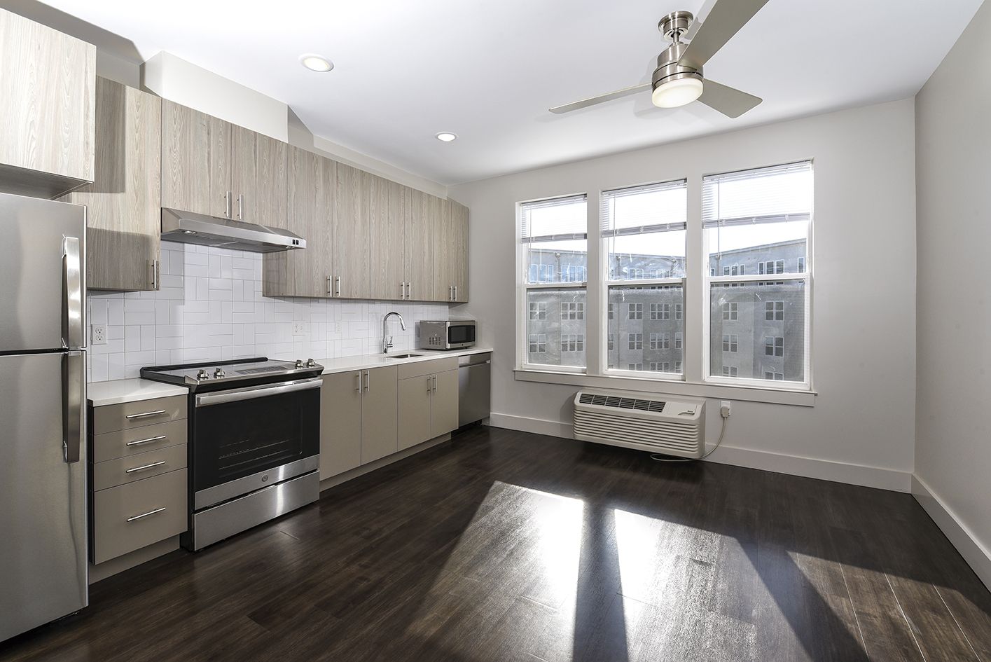 Modern kitchen with light wood cabinets, stainless steel appliances, and large windows.