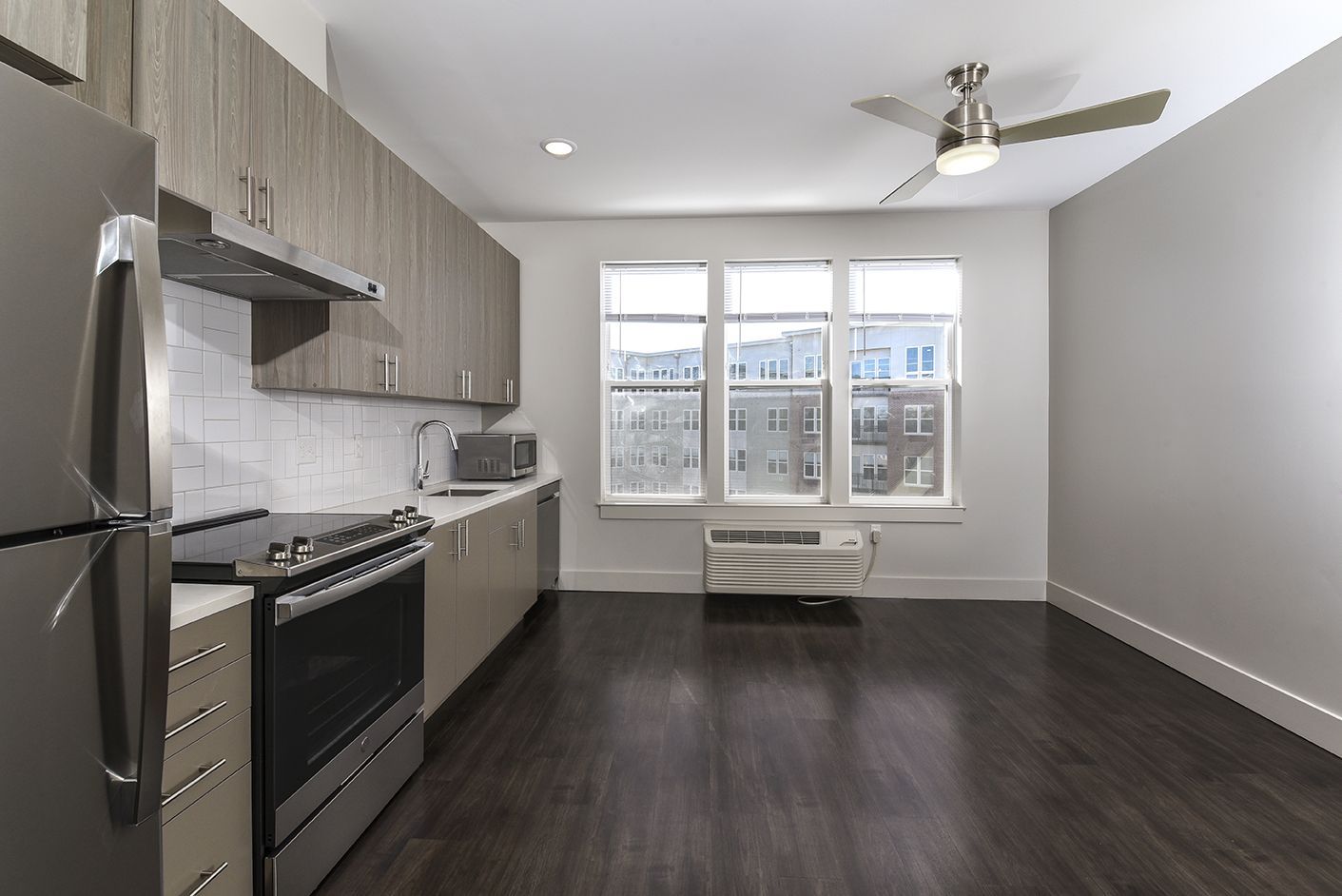 Modern kitchen with dark wood floors, stainless steel appliances, and large windows.