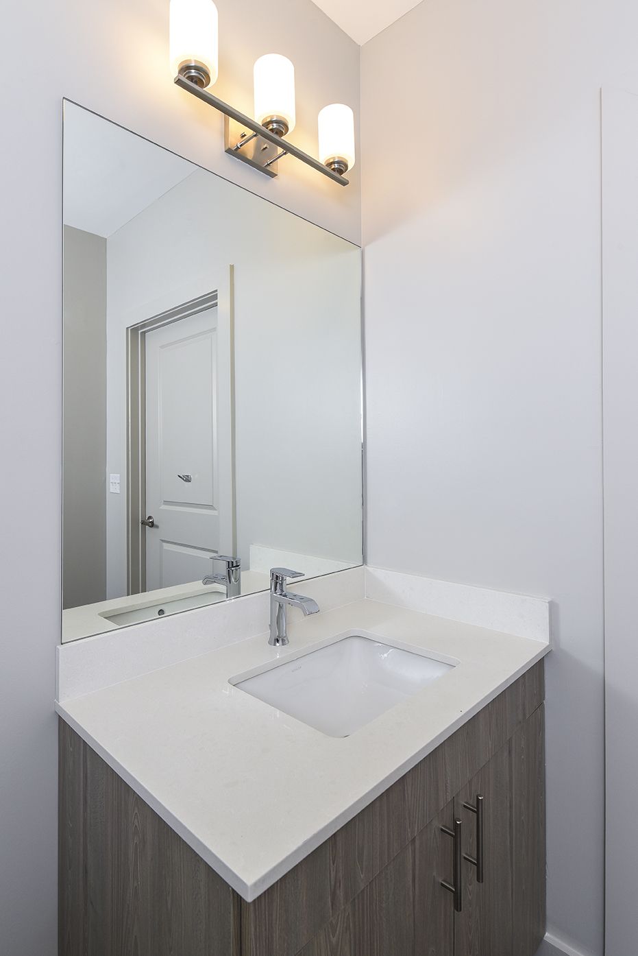 Bathroom vanity with white countertop, square sink, large mirror, and three-light fixture.