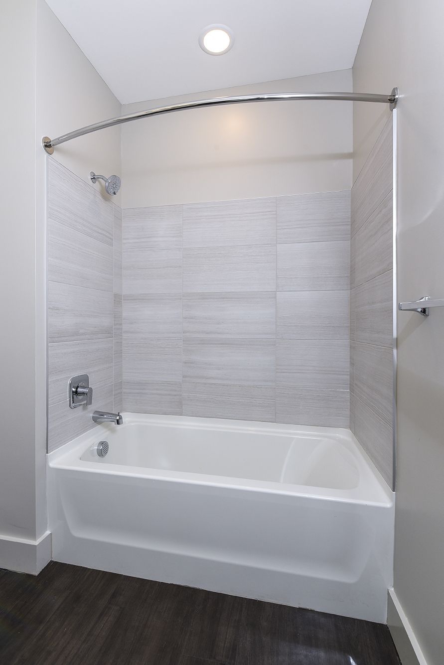 White bathtub and tiled shower with curved shower rod in a modern bathroom.