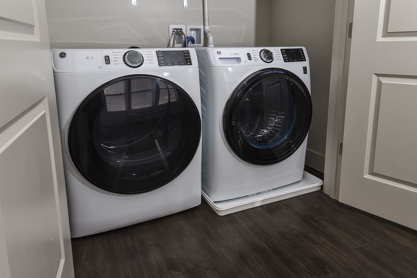 White washer and dryer appliances in a laundry room, set on a platform.