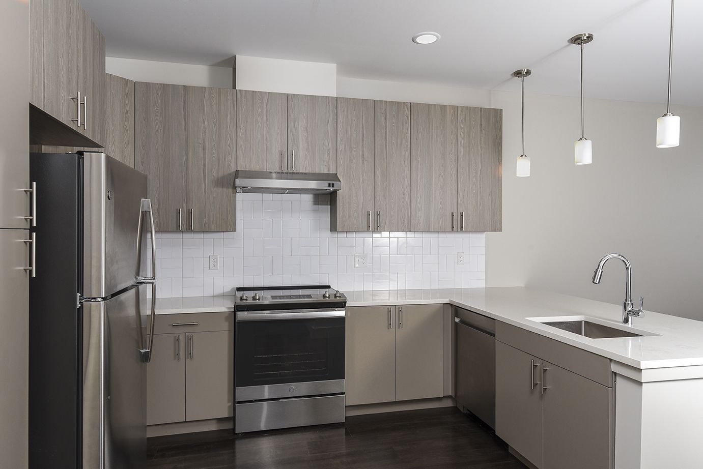Modern kitchen with stainless steel appliances, light wood cabinets, white countertops, and pendant lights.