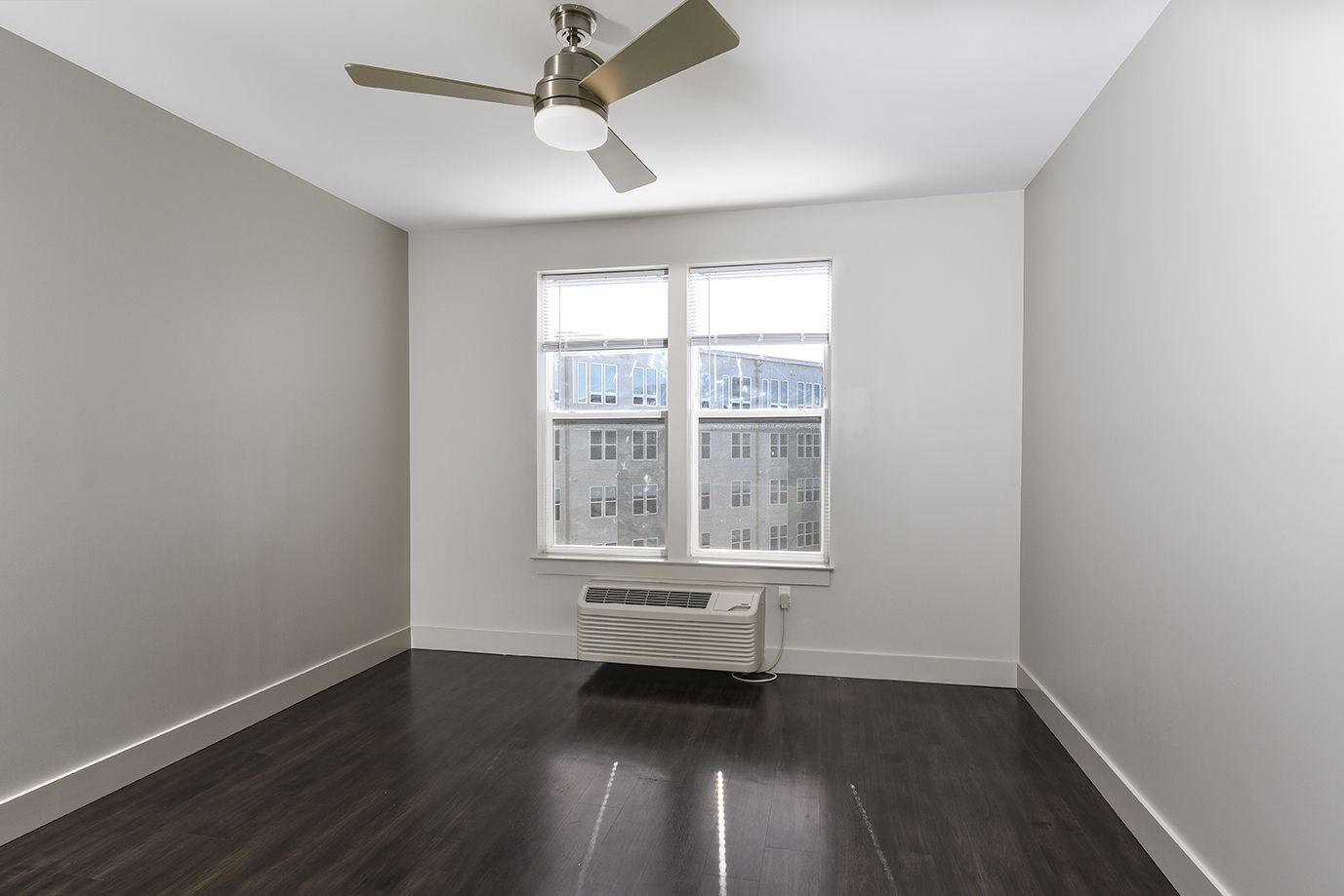 Empty room with dark wood floor, window, ceiling fan, and beige walls.