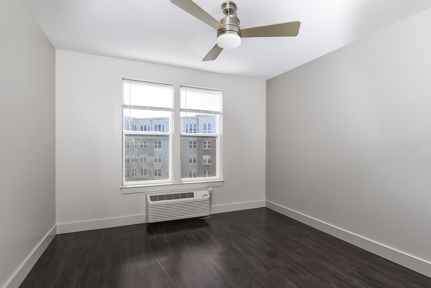 Empty bedroom with dark wood floor, a window with an AC unit, and a ceiling fan.