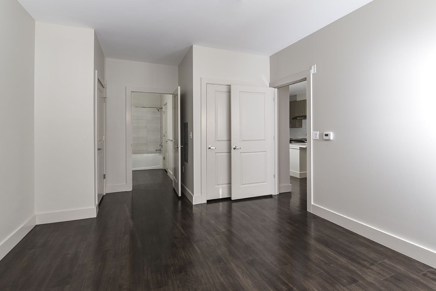 Empty room with dark wood floors, white walls, and open doors to other rooms.