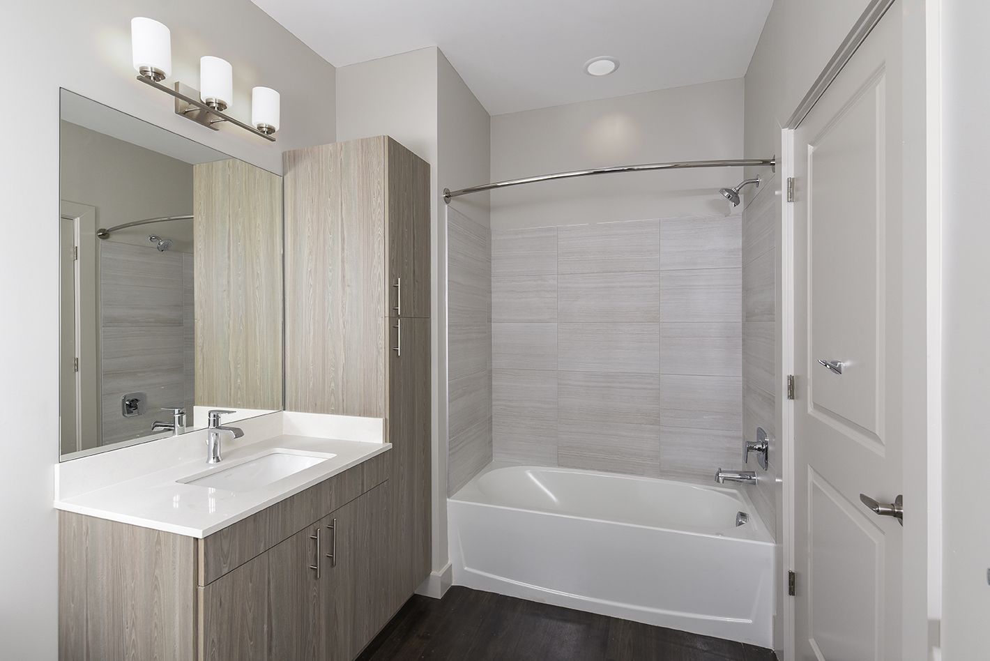 Modern bathroom with white countertops, gray wood cabinets, and a white bathtub.