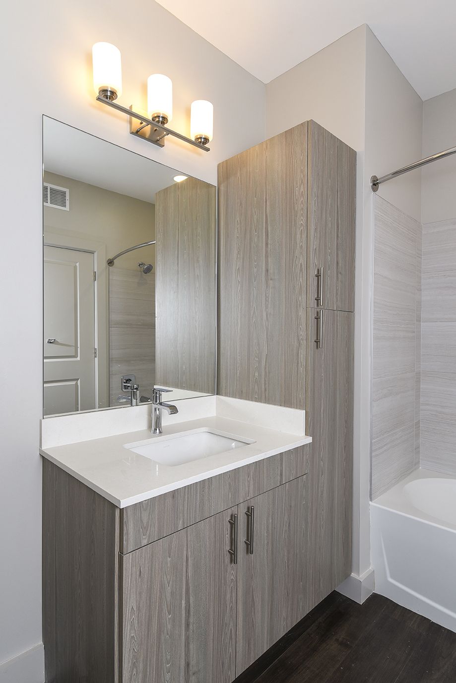 Bathroom with gray wood vanity, white countertop, large mirror, and three-bulb light fixture.