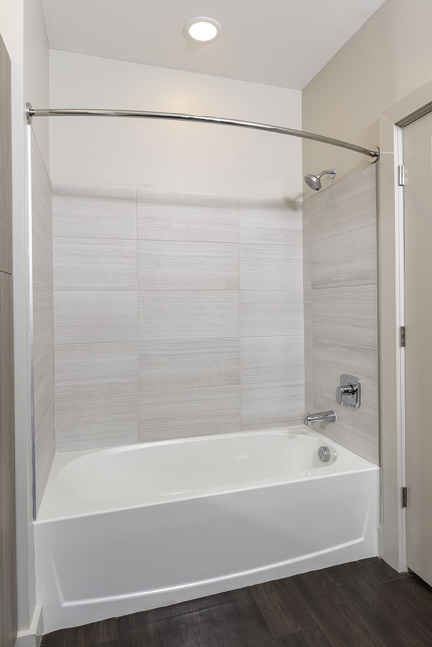 White-tiled bathroom with a white bathtub and silver shower fixtures.
