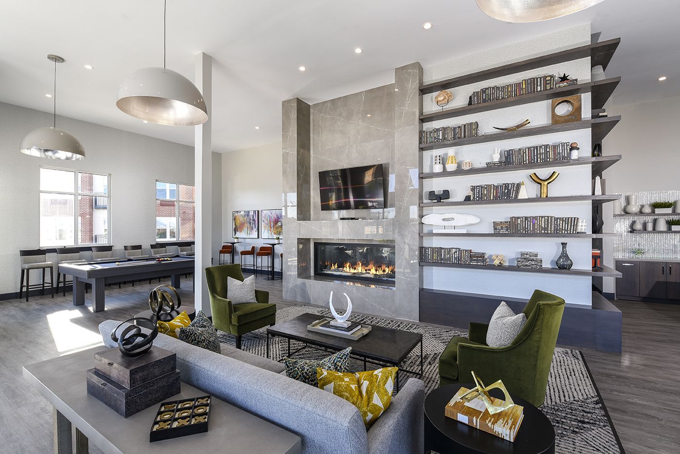 Spacious modern living room with fireplace, bookshelves, seating, and pool table in the background.