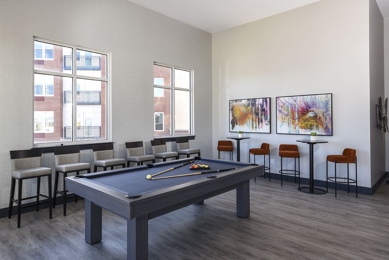 Pool table in a game room with bar stools, artwork, and windows.