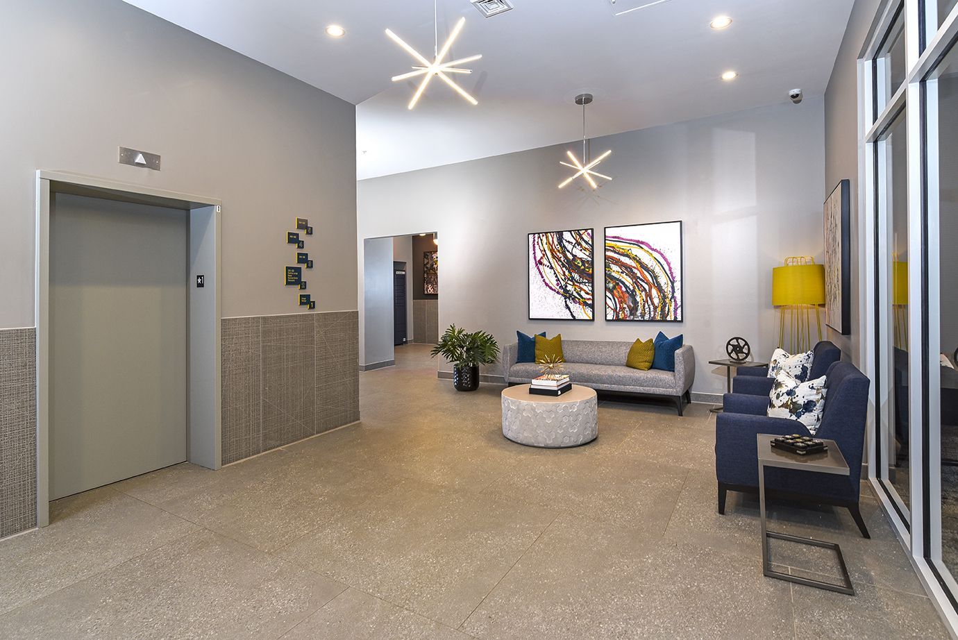Modern lobby with seating area, elevator, abstract art, and decorative lighting.