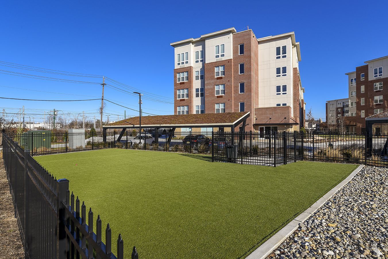 Dog park with artificial turf, fenced area, and apartment building in the background.