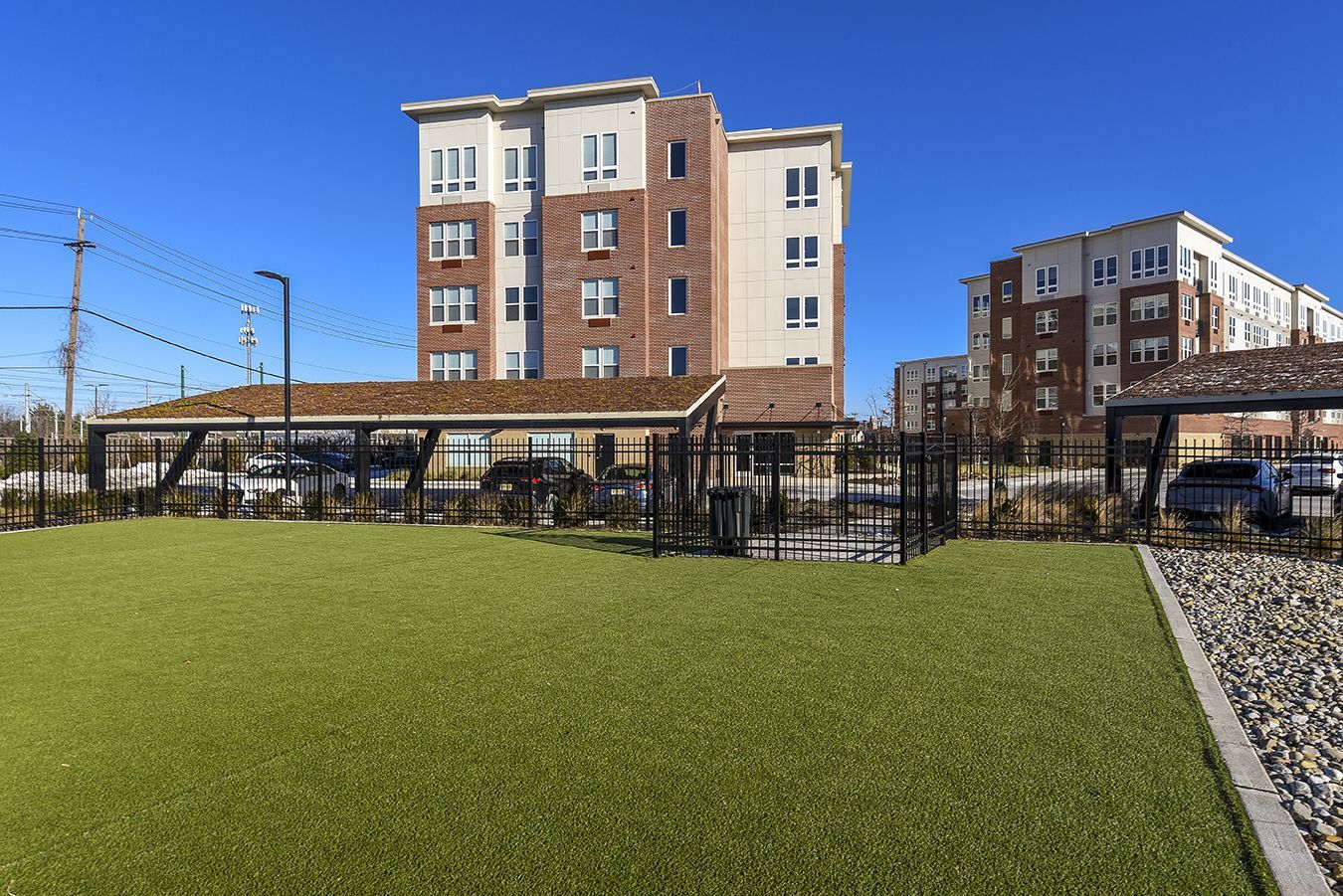 Apartment buildings with a fenced dog park and green turf on a sunny day.