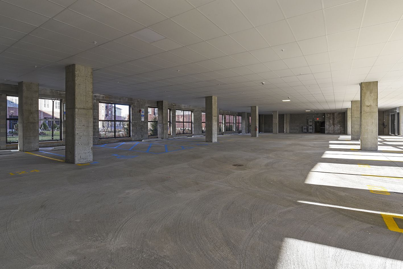 Empty, open concrete parking garage with support columns, windows along one side, and yellow parking space markings.