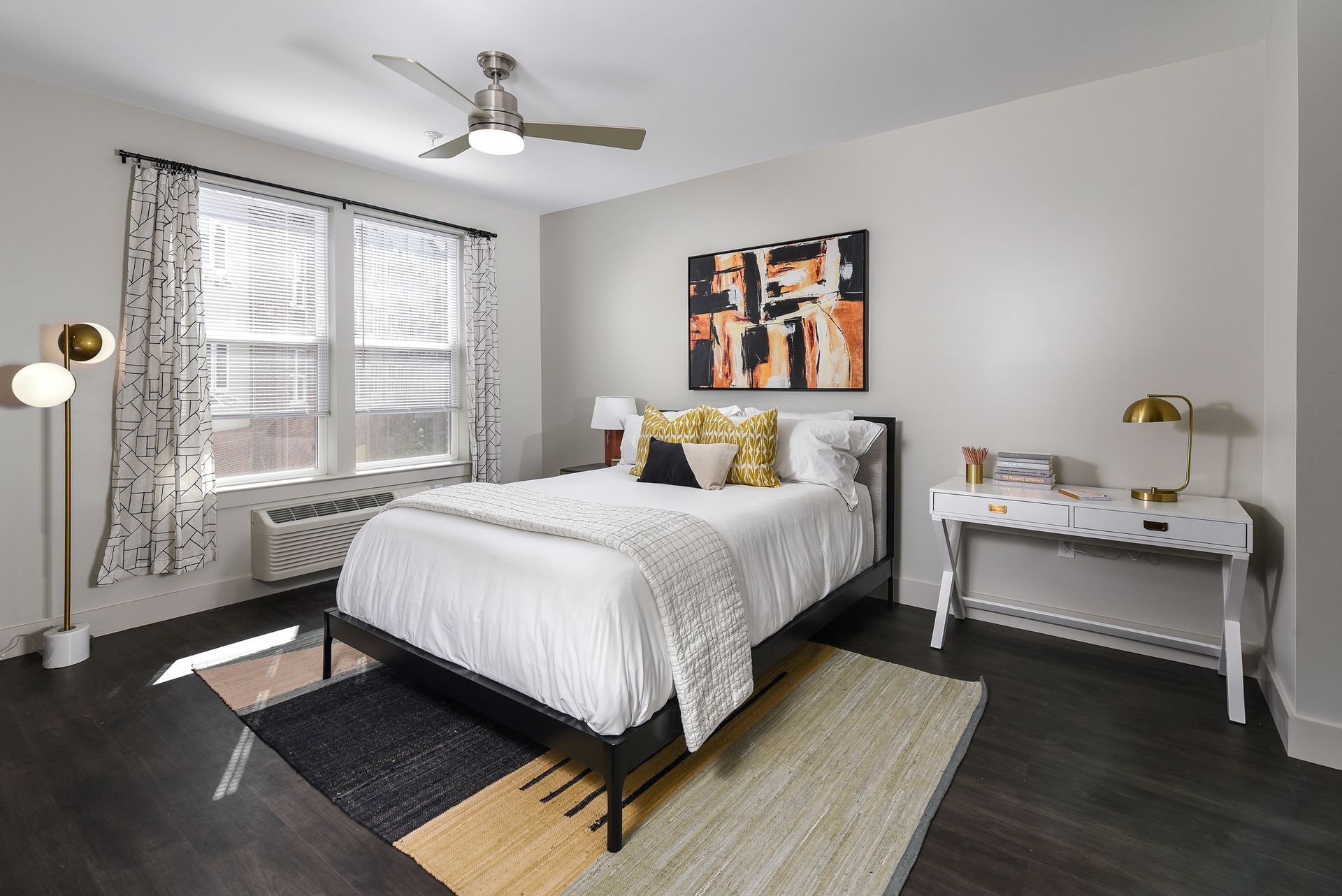 Bedroom with bed, desk, window, and decorative art. Neutral color scheme, dark wood floor.