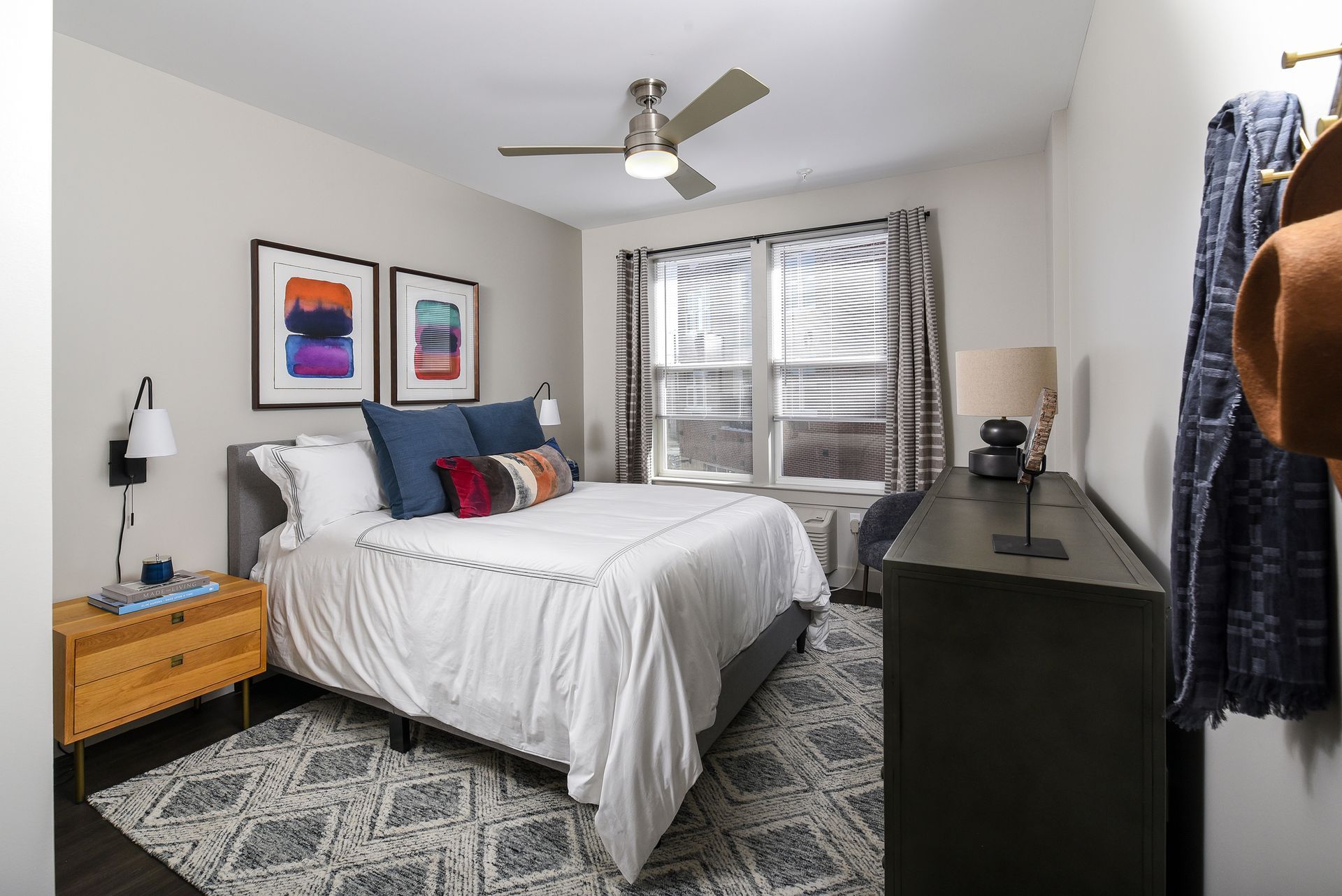 Bedroom with bed, nightstand, dresser, artwork, and window. Neutral colors and patterned rug.
