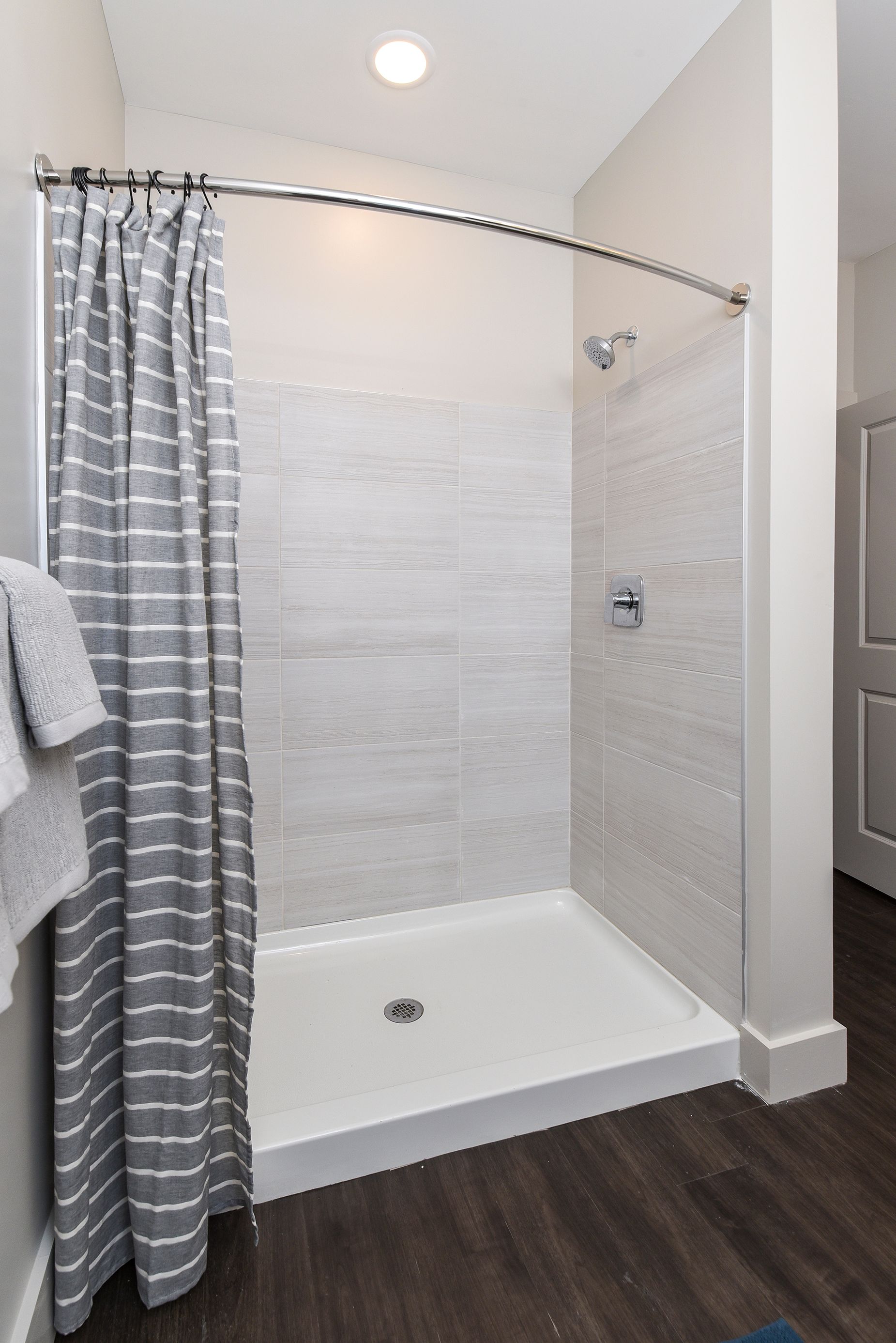 Shower with white and gray tiled walls, silver fixtures, and gray striped curtain.