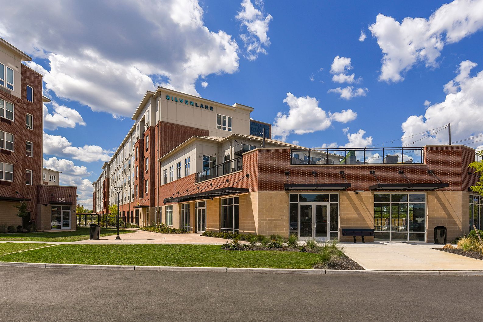 Multi-story brick and beige building with large windows under a blue sky with clouds.