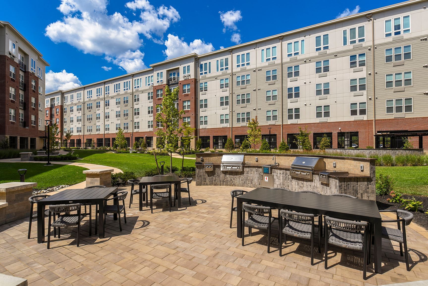 Outdoor patio with grills, tables, and apartment building in the background on a sunny day.