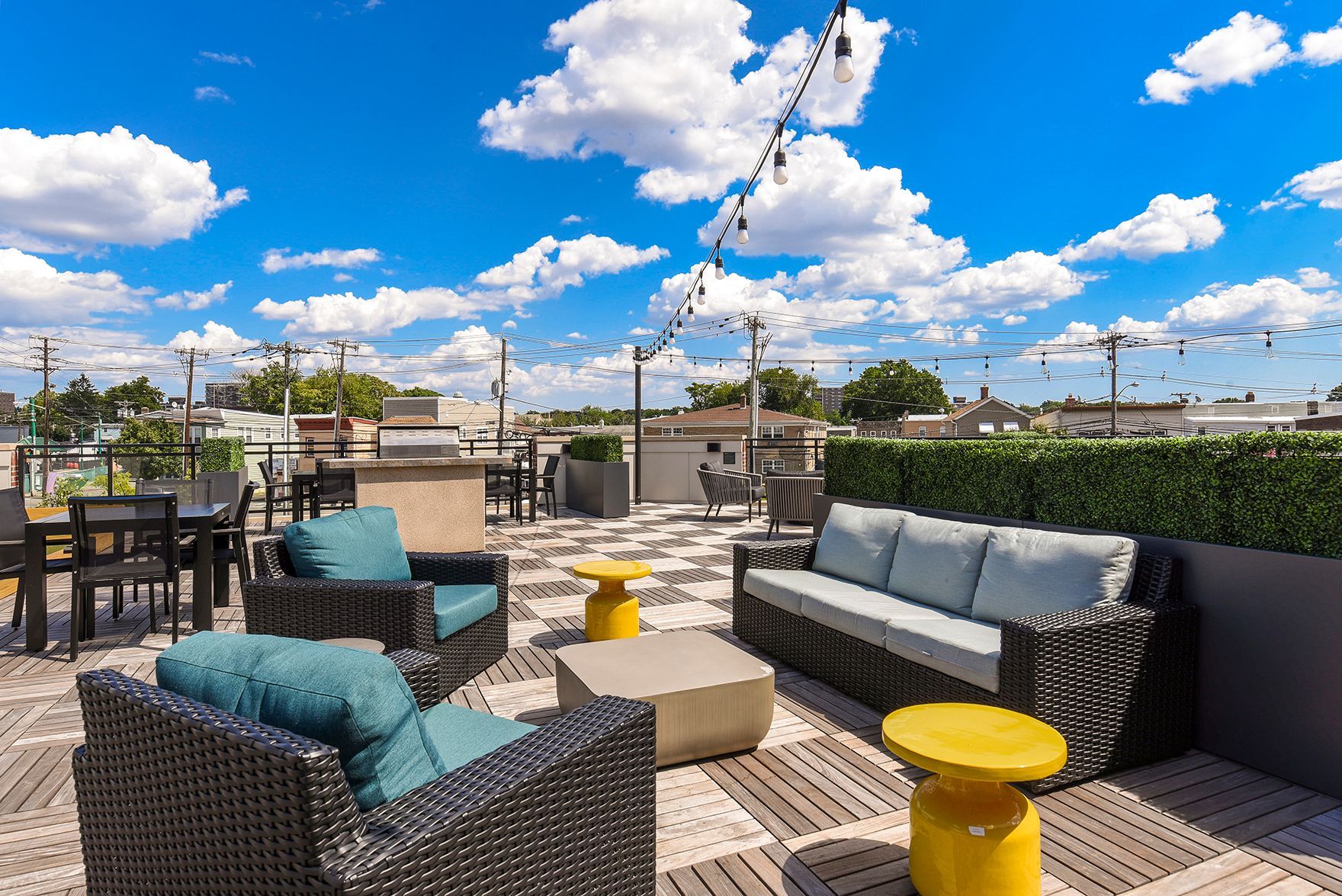 Rooftop patio with seating, grilling area, and string lights against a blue sky with clouds.