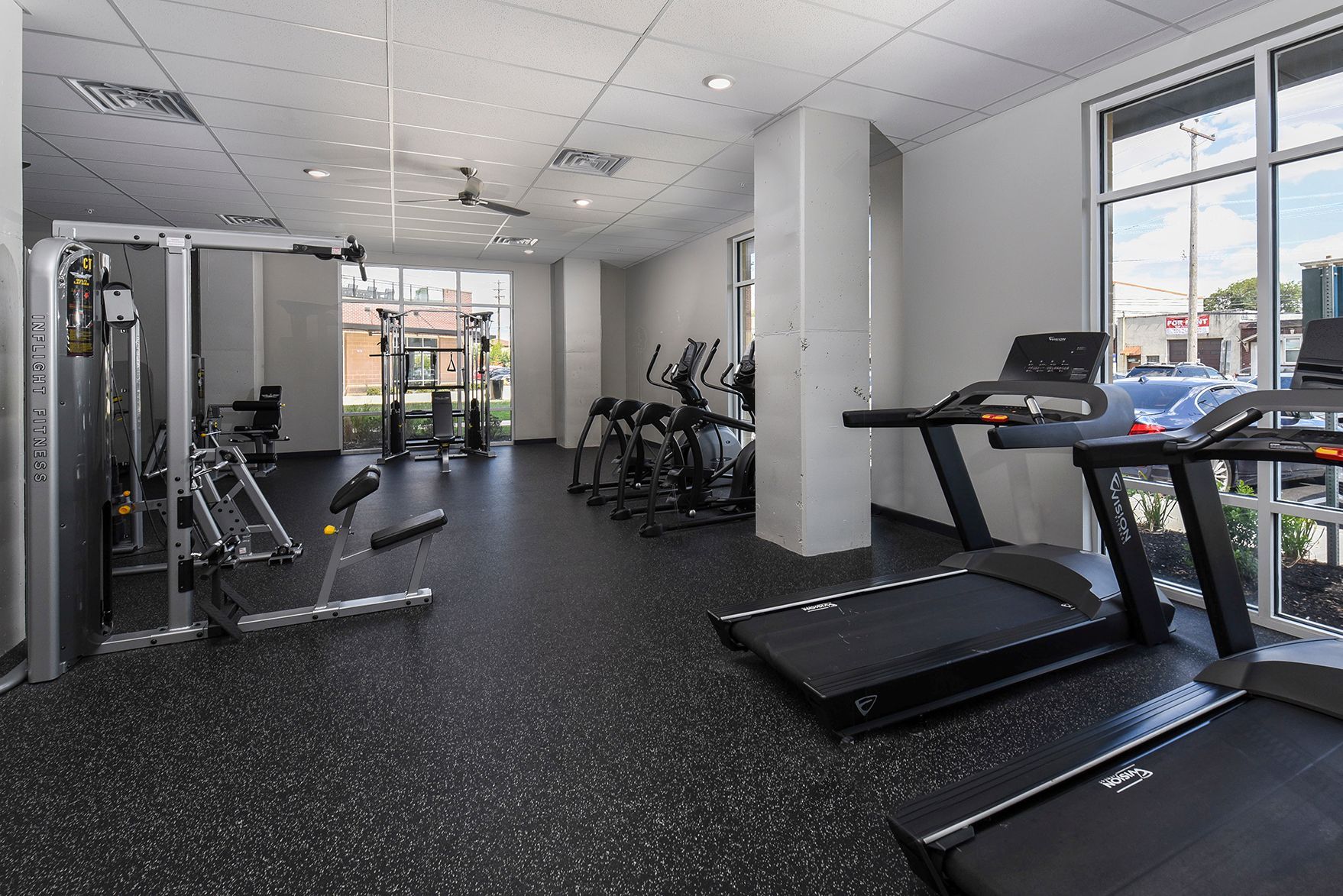 Gym with treadmills, weight machines, and elliptical machines; windows along the wall.