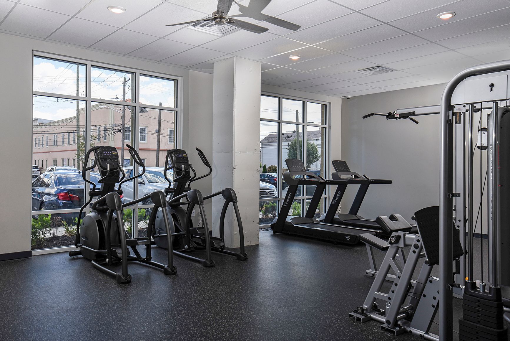 Gym with cardio machines and weight equipment, near windows with a view of a street.