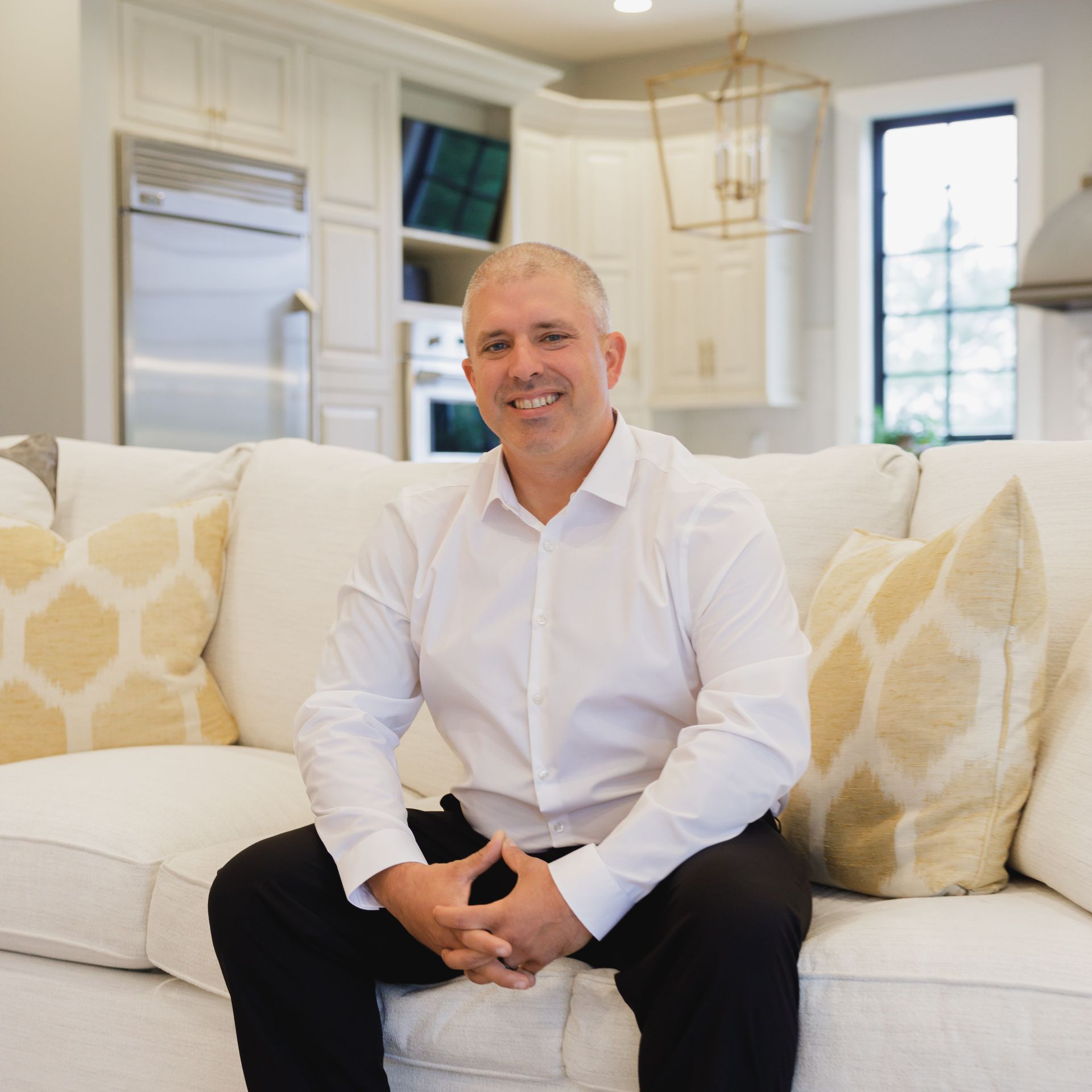 A man in a white shirt is standing in a kitchen next to a window.