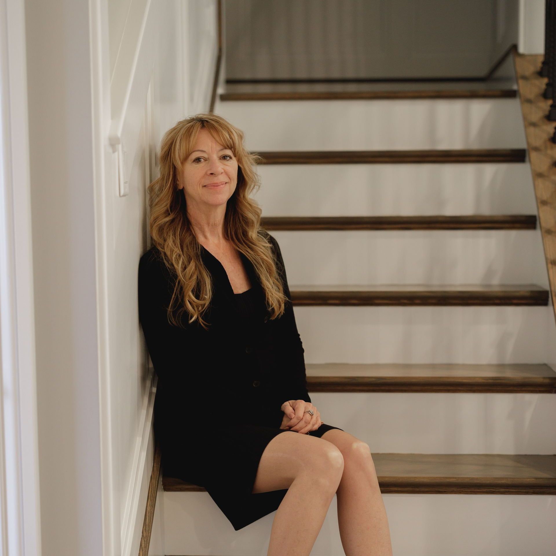 A woman in a black dress is sitting on a set of stairs.