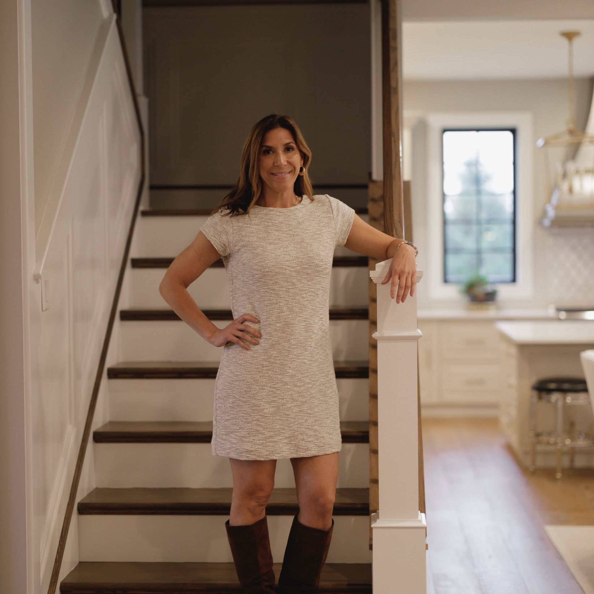 A woman in a white dress and brown boots is standing on a set of stairs.